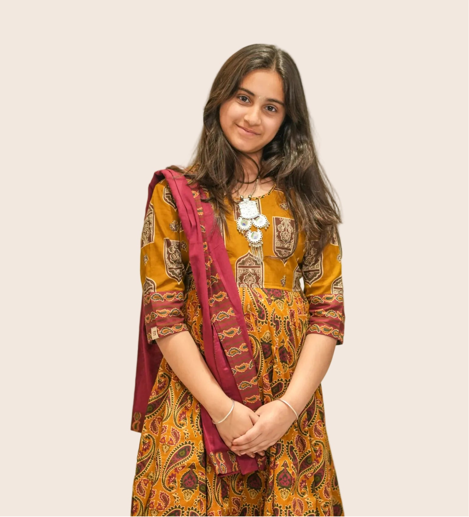 Girl wearing a traditional outfit with a yellow and red patterned dress in an indoor setting.
